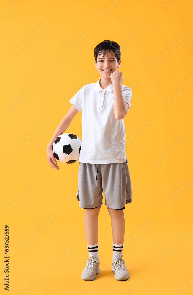 Happy little boy with soccer ball on yellow background