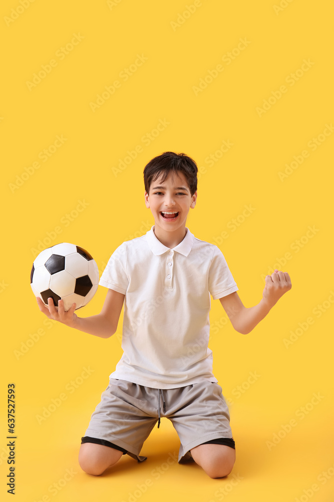 Happy little boy with soccer ball on yellow background