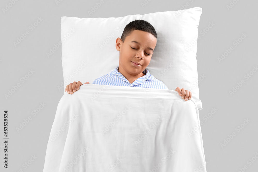 Little African-American boy with soft blanket and pillow on light background