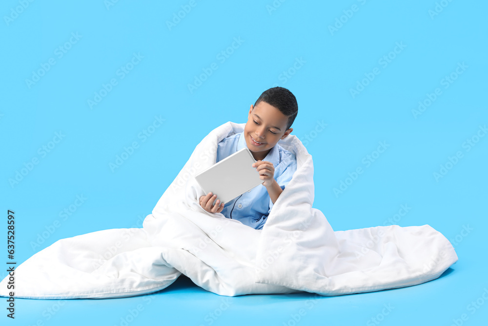 Little African-American boy with soft blanket using tablet computer on blue background