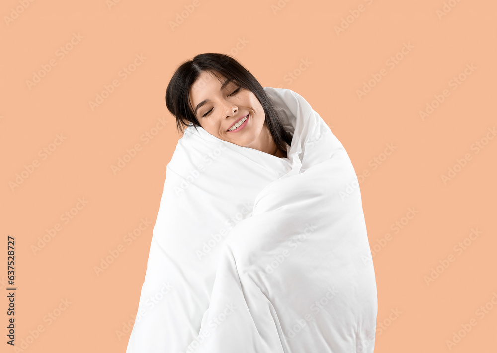 Beautiful happy young woman with soft blanket sleeping on pale orange background