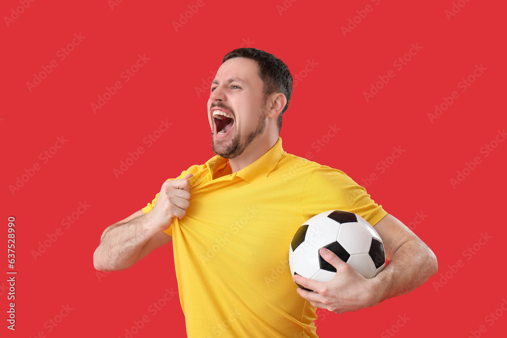 Emotional man with soccer ball on red background