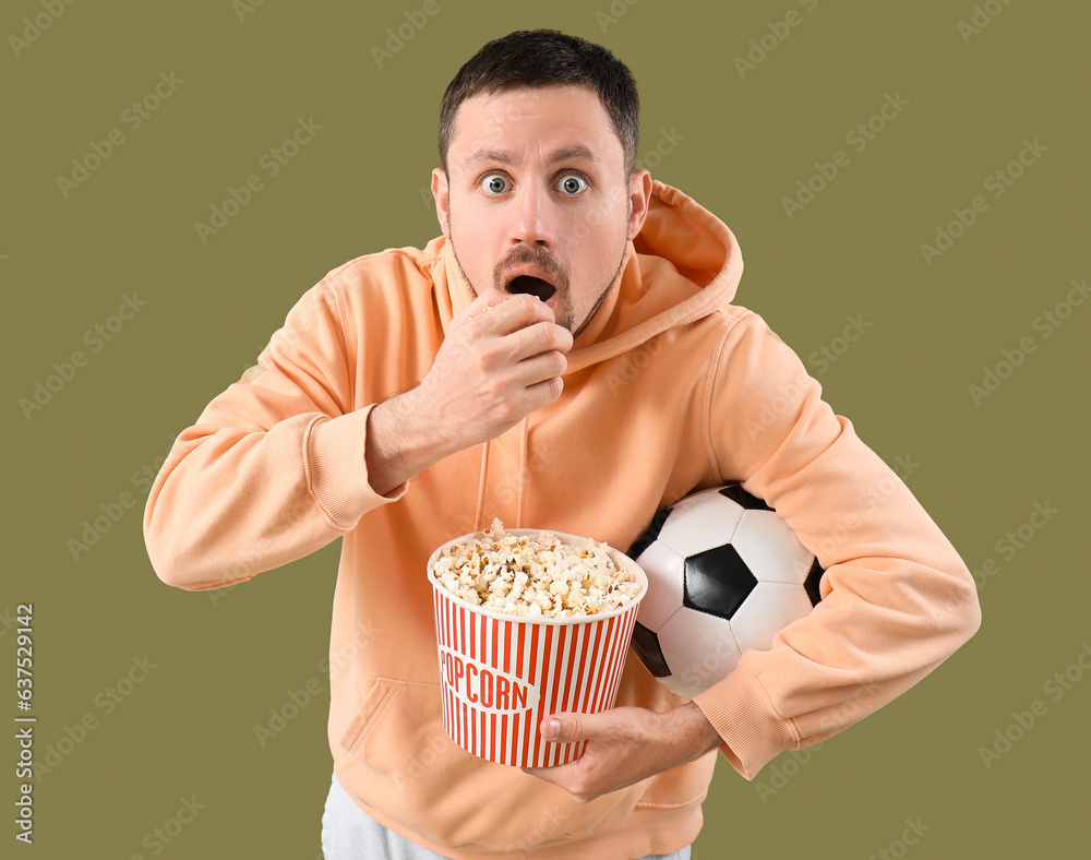 Shocked soccer fan with ball and popcorn on color background