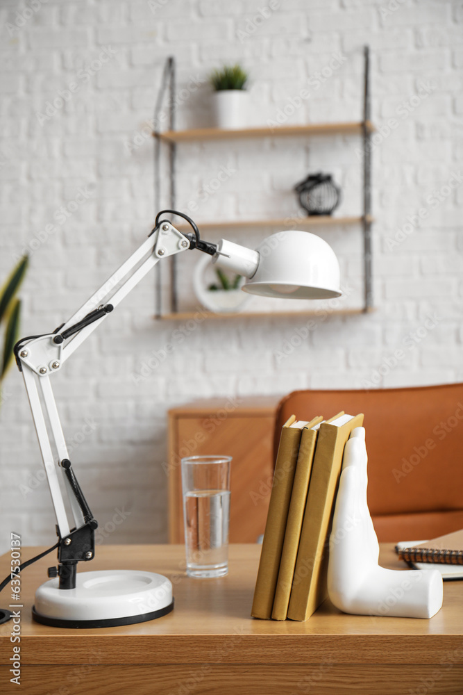 Workplace with laptop, stylish holder for books and lamp in room