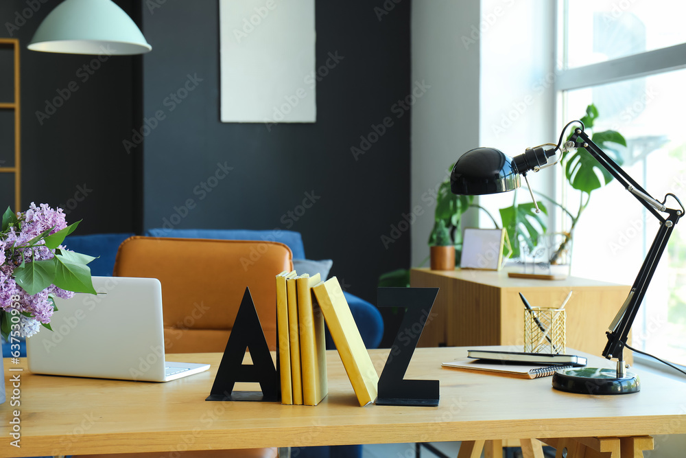 Stylish holder for books with laptop and lamp on table in room