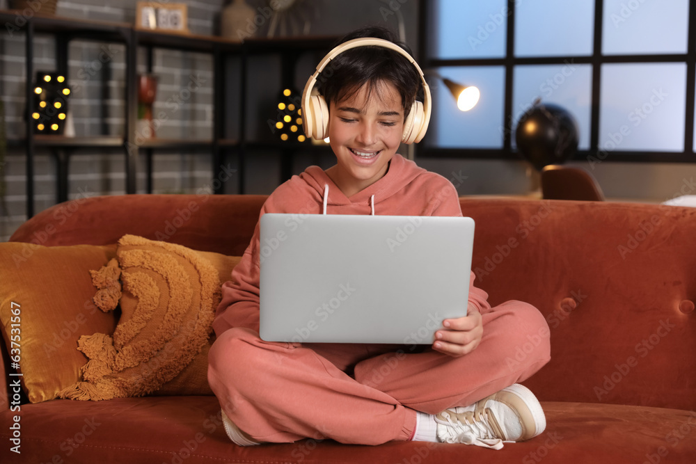 Little boy with headphones using laptop at home late in evening