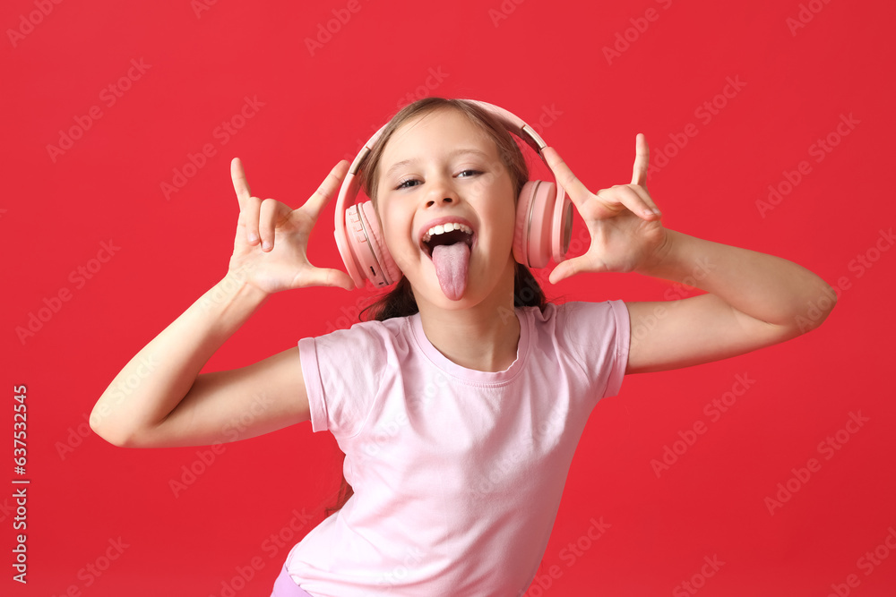 Little girl in headphones showing  devil horns  on red background