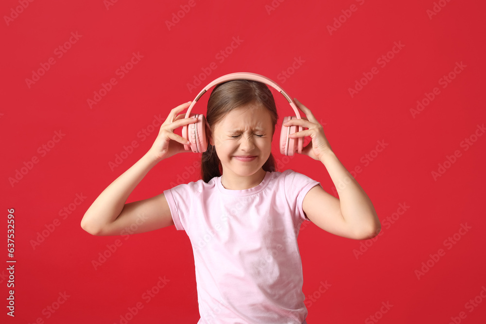 Displeased little girl with headphones on red background