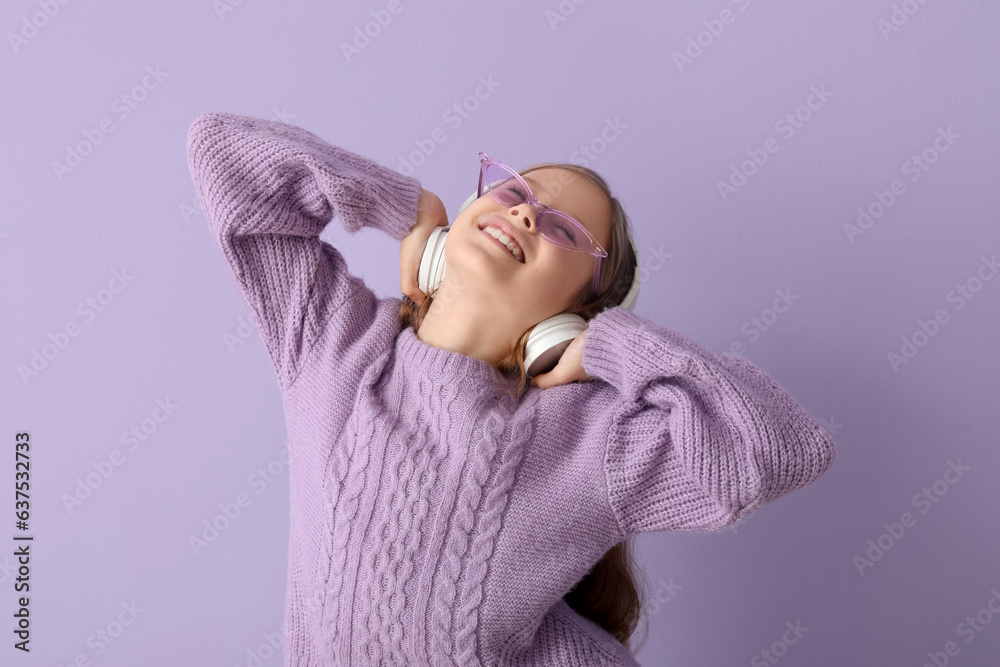 Little girl in headphones listening to music on lilac background