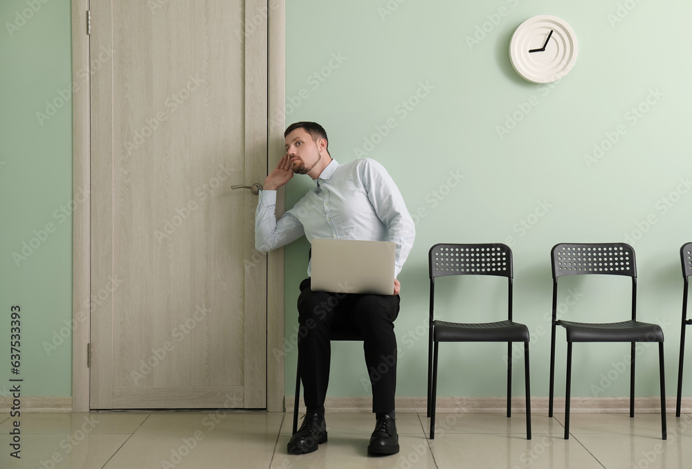 Male applicant with laptop trying to hear something before job interview in room