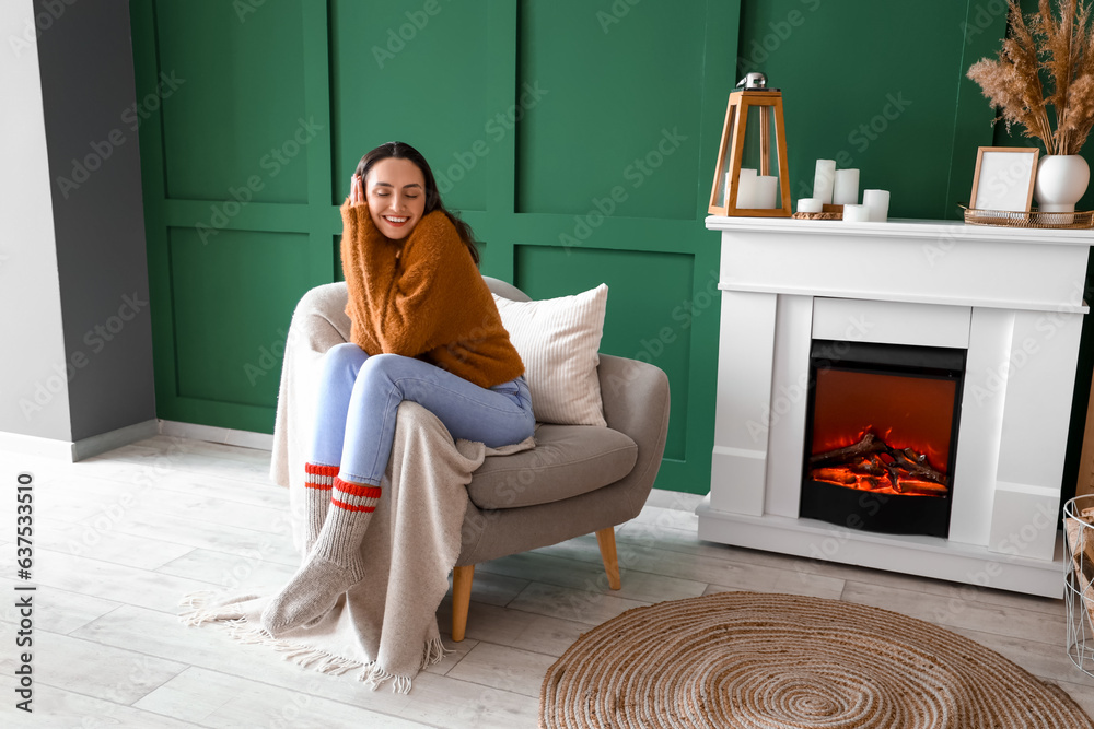 Young woman sitting in armchair near fireplace at home