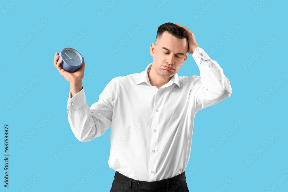 Stressed businessman with clock on blue background. Deadline concept