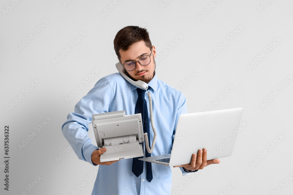 Young businessman with laptop talking by telephone on light background. Deadline concept