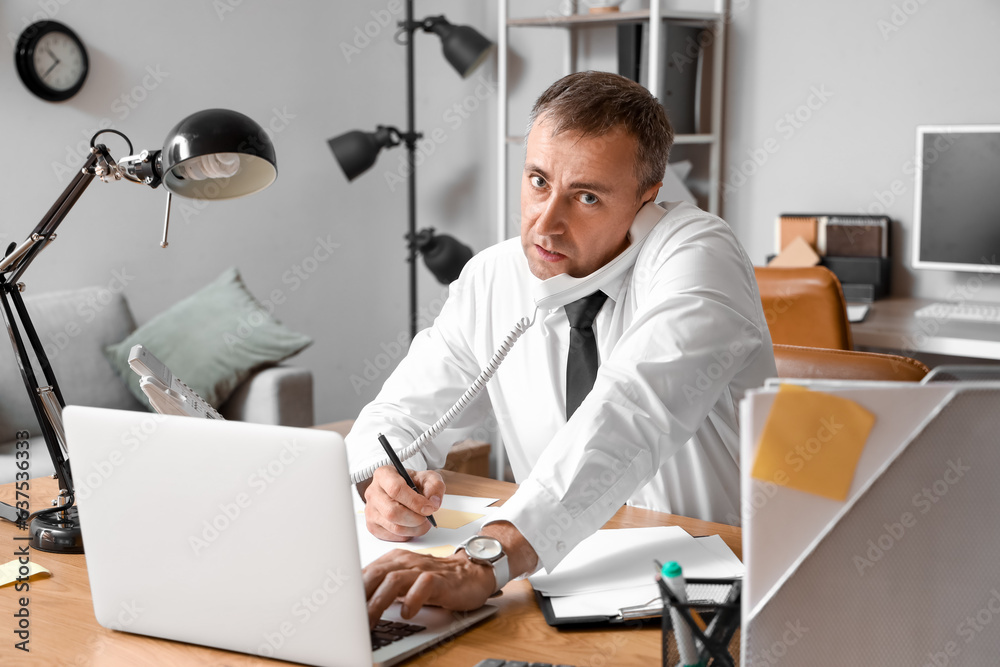 Stressed mature businessman working under deadline in office