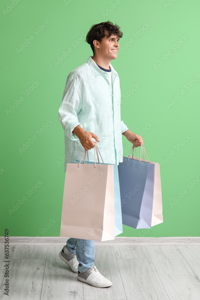 Young man with shopping bags near green wall