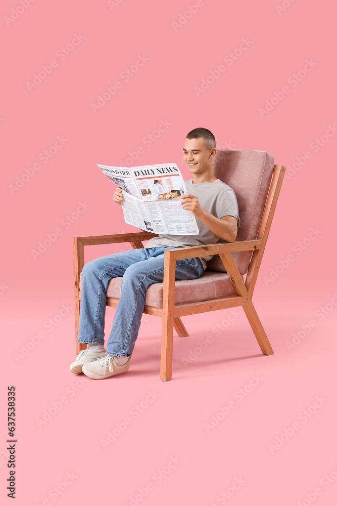 Happy young man sitting on chair and reading newspaper against pink background