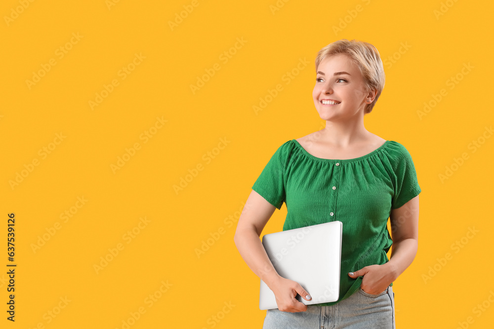 Happy young female programmer with laptop on yellow background