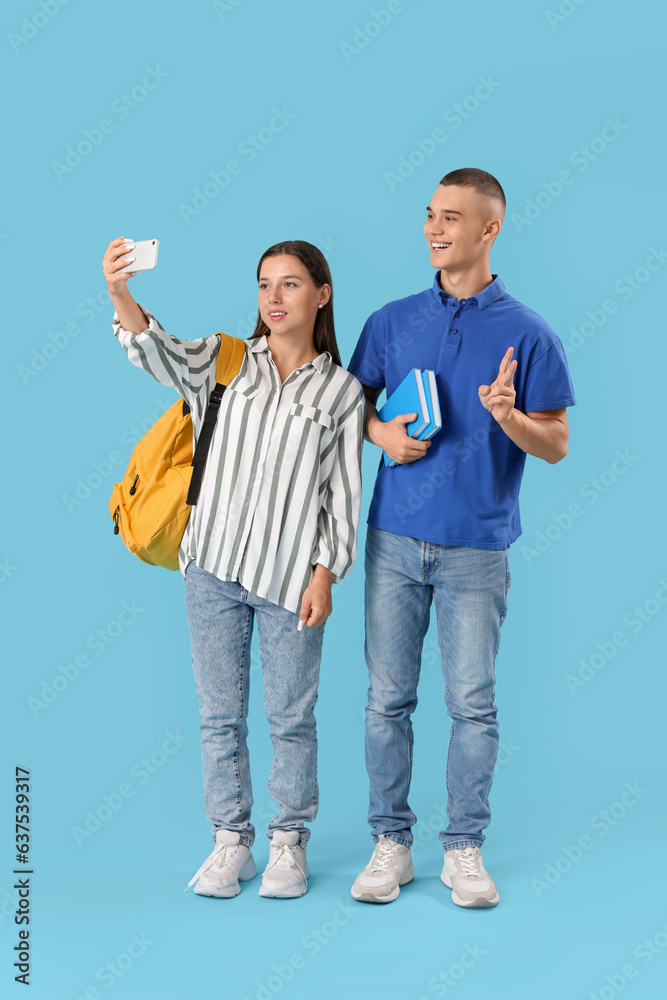 Happy students with backpack and books taking selfie on blue background