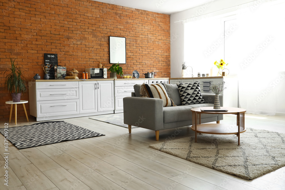 Interior of modern open space kitchen with grey sofa, coffee table and white counters