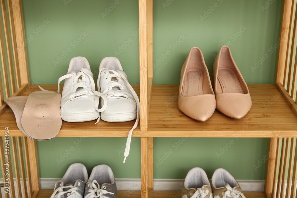 Wooden shoe rack with shoes and orthopedic insoles near color wall, closeup