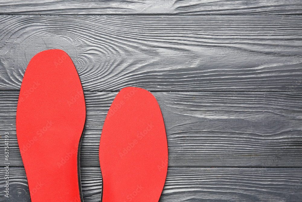 Pair of red orthopedic insoles on dark wooden background, closeup