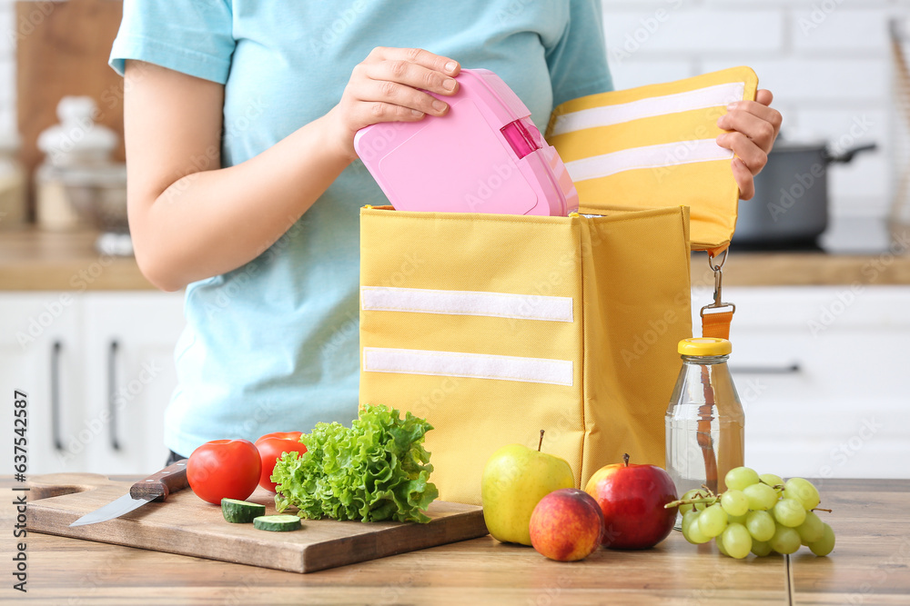 Woman packing fresh meal into lunch box bag in kitchen