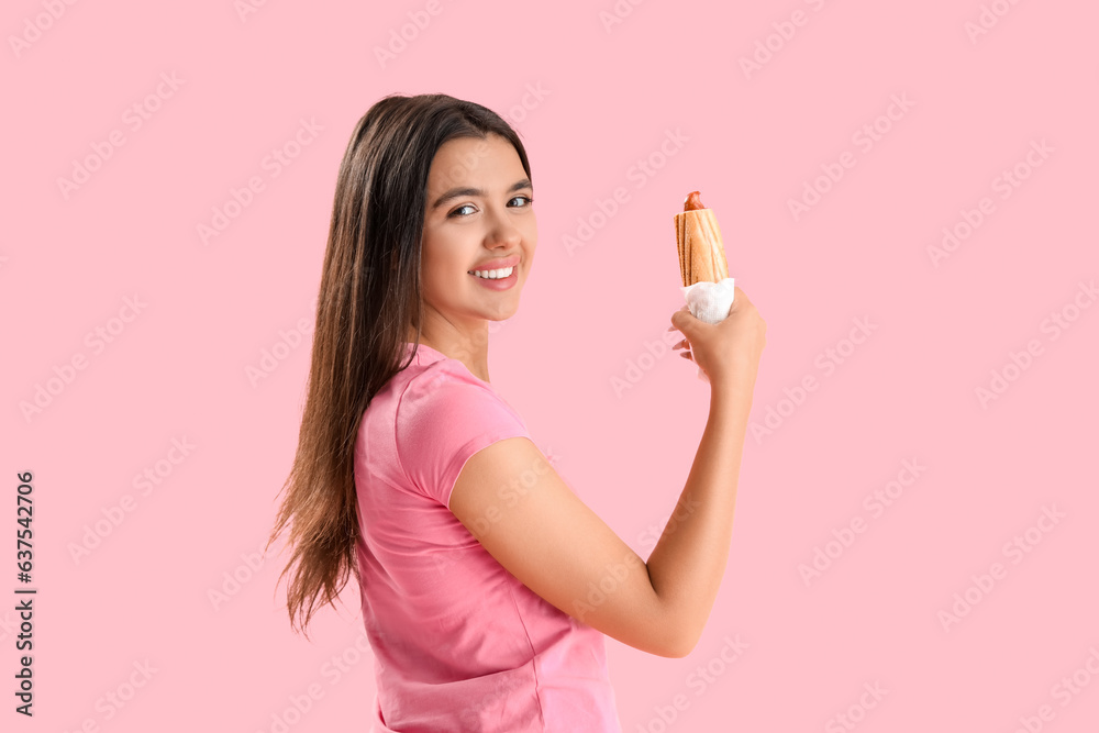 Pretty young woman with tasty french hot dog on pink background