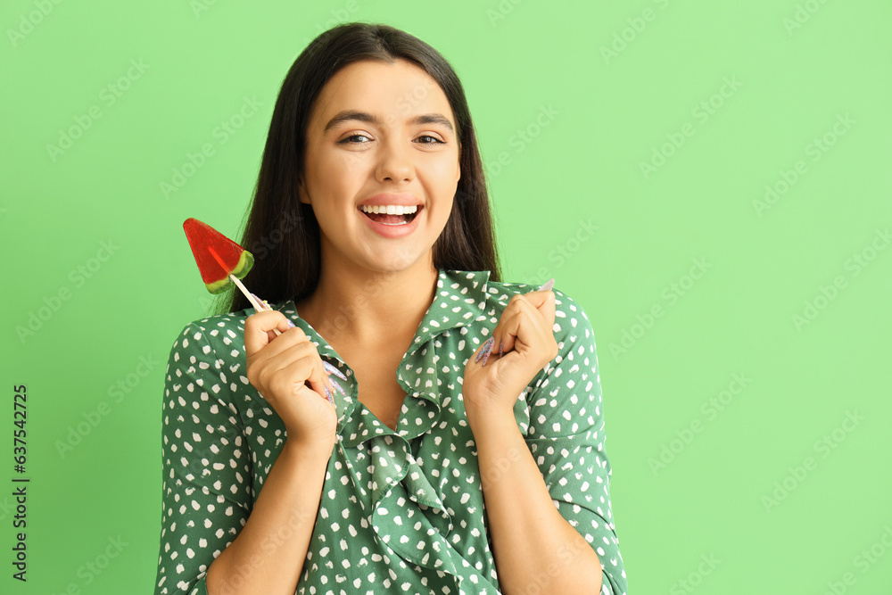 Beautiful happy young woman with watermelon lollipop on green background