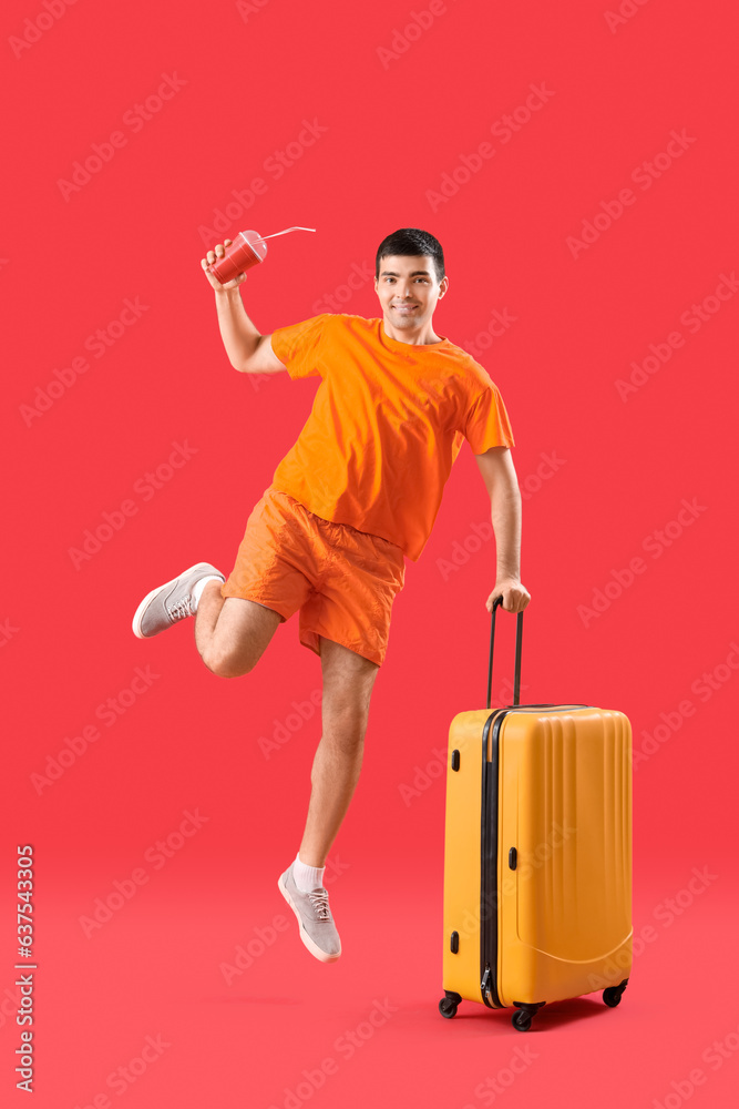 Jumping male tourist with suitcase and drink on red background