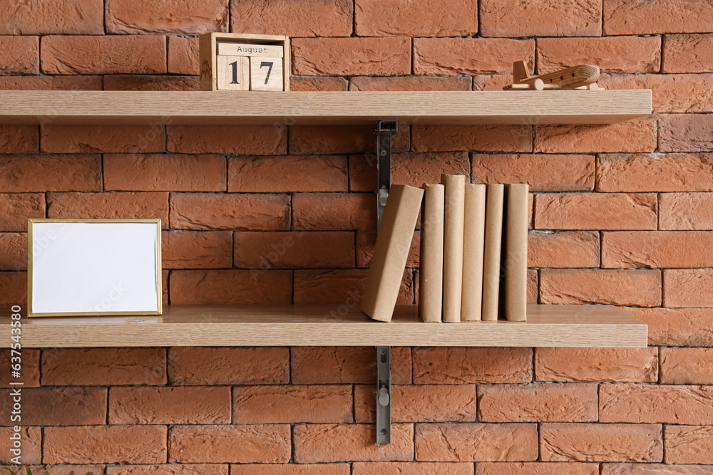 Shelf with books, frame and calendar on brick wall