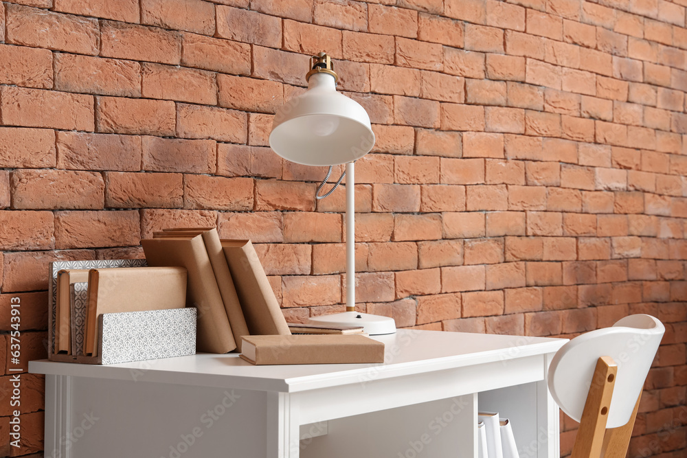 Table with books and lamp near brick wall