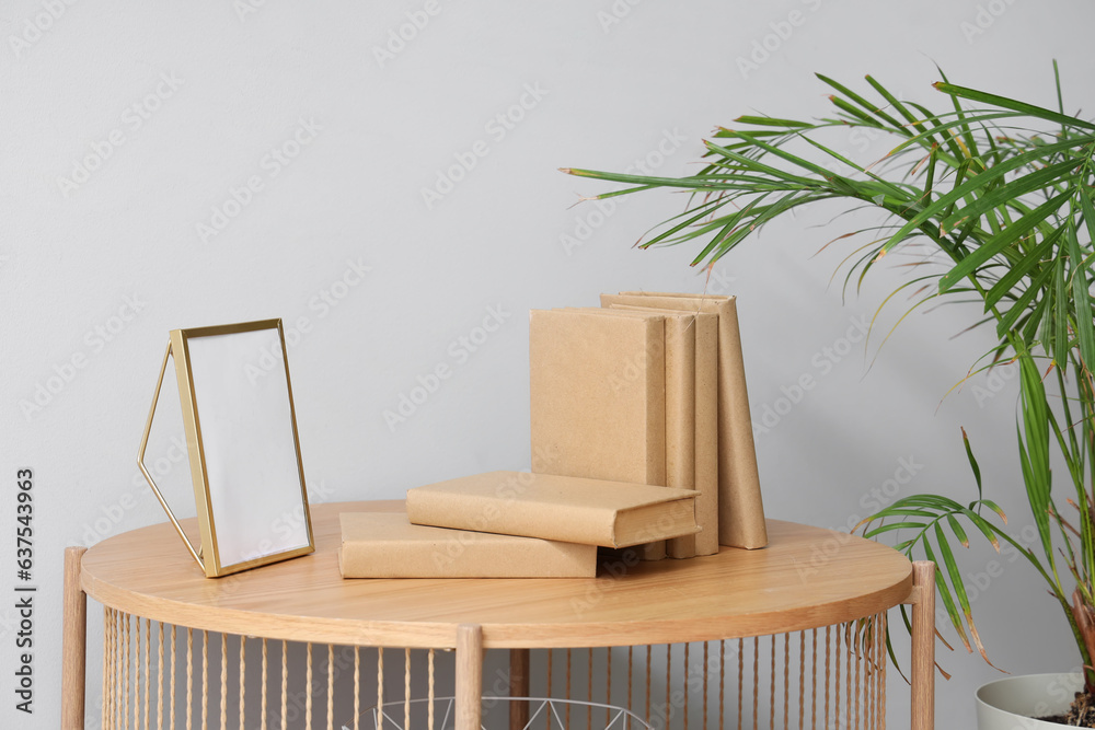 Books with blank frame on table near light wall