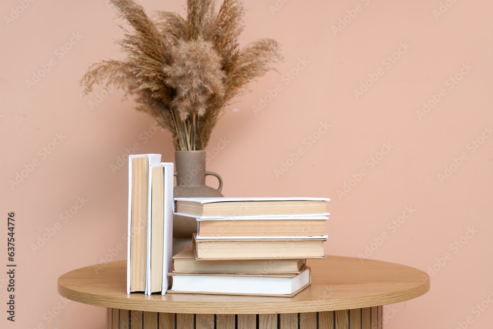 Books and vase with pampas grass on table near beige wall