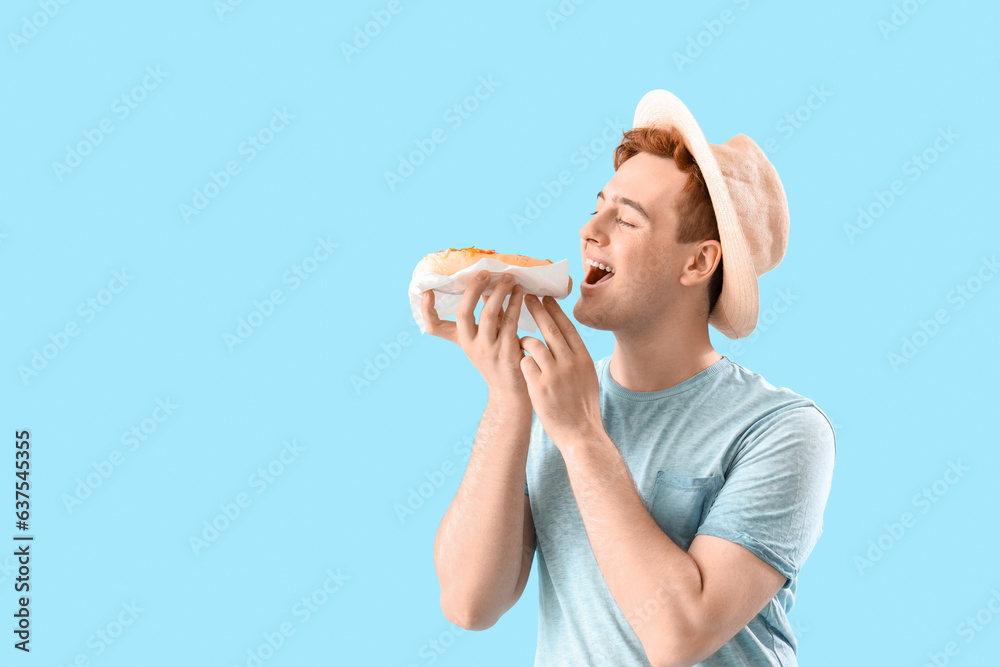 Young man with tasty hot dog on light blue background