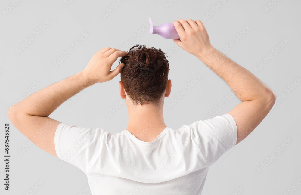 Young man applying shampoo to his hair against light background, back view