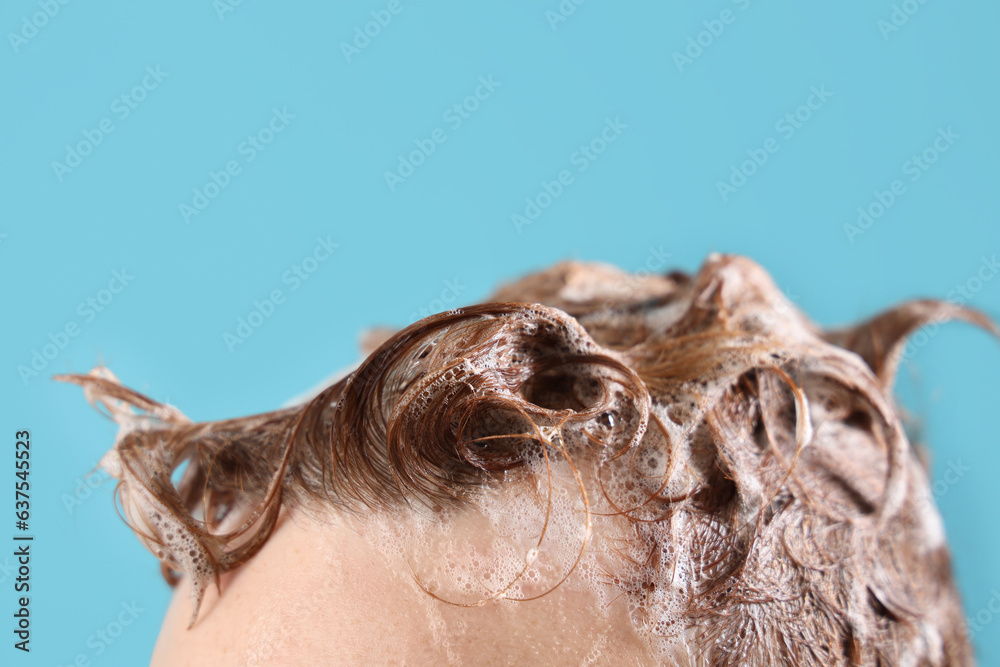 Young man with applied shampoo on his hair against light blue background