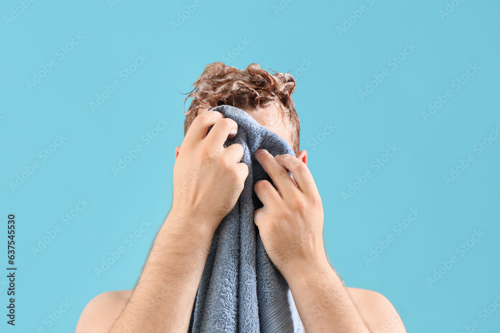 Young man wiping his face during washing hair against light blue background