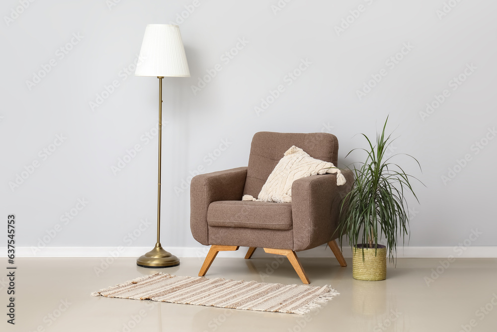 Cozy armchair with cushion and standard lamp near white wall