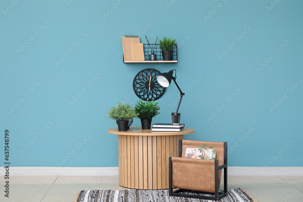 Desk lamp and houseplants on small wooden table near blue wall