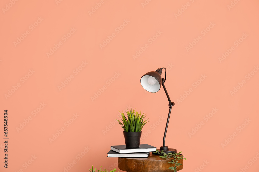 Desk lamp and houseplant on small wooden table near pink wall