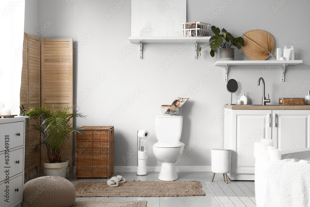 Interior of light restroom with ceramic toilet bowl, sink and vanity cabinets