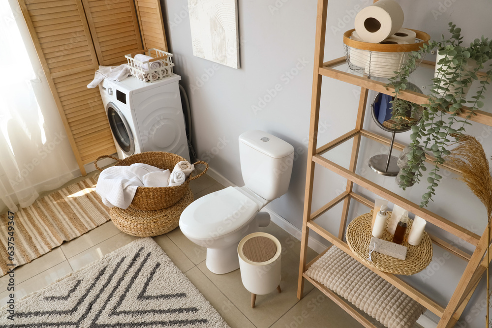 Interior of light restroom with ceramic toilet bowl, shelving unit and washing machine