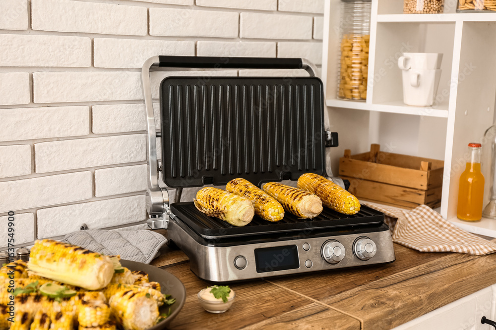 Electric grill with tasty corn on wooden kitchen counter