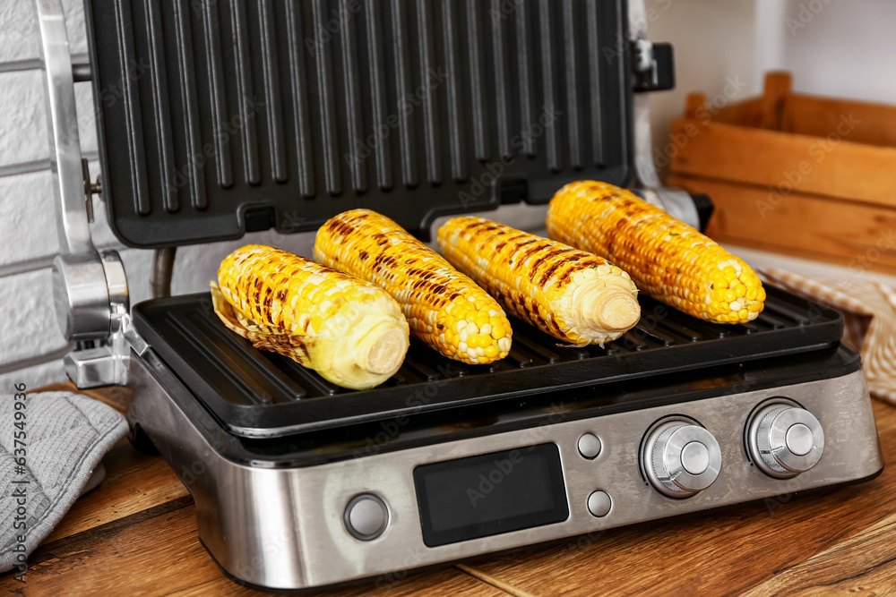 Electric grill with tasty corn on wooden kitchen counter