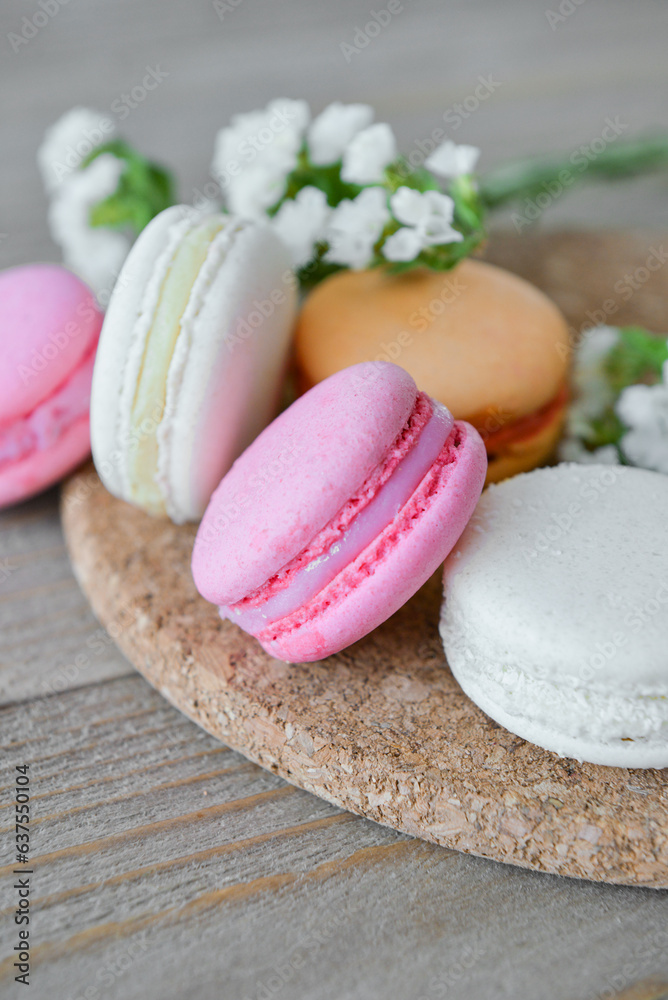 Board with sweet macaroons and beautiful flowers on grey wooden background