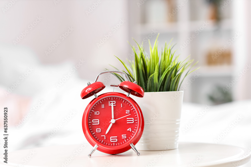 Alarm clock and houseplant on table in bedroom, closeup