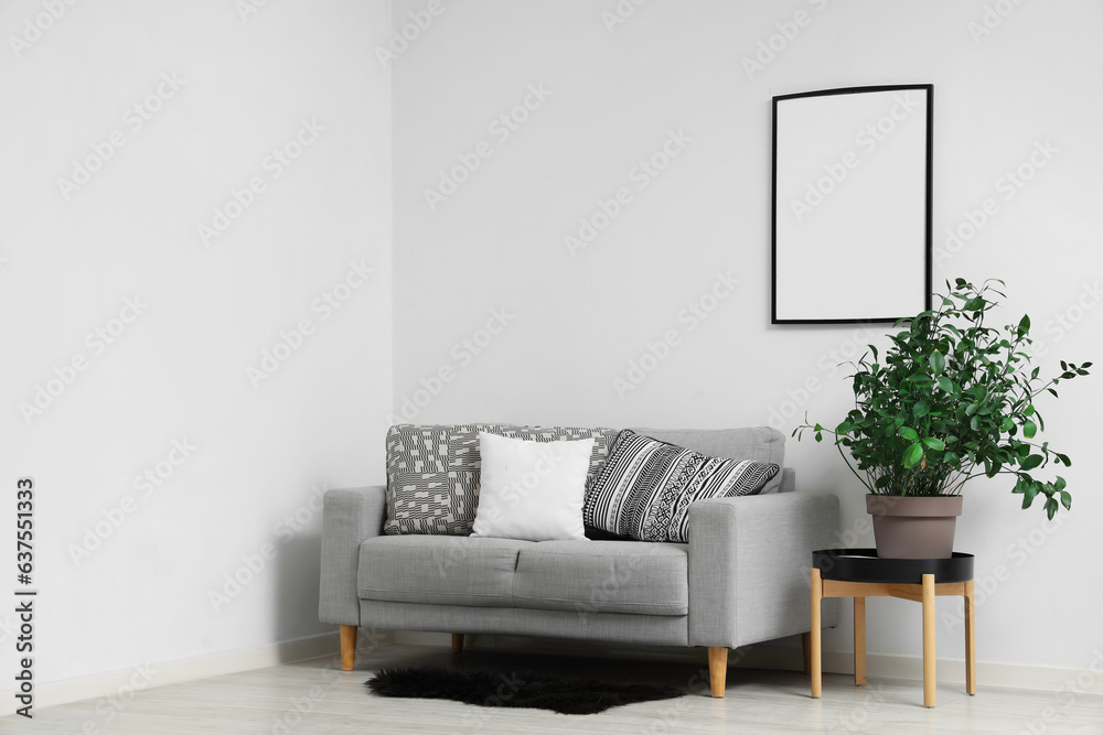 Interior of light living room with blank frame, grey sofa and houseplant