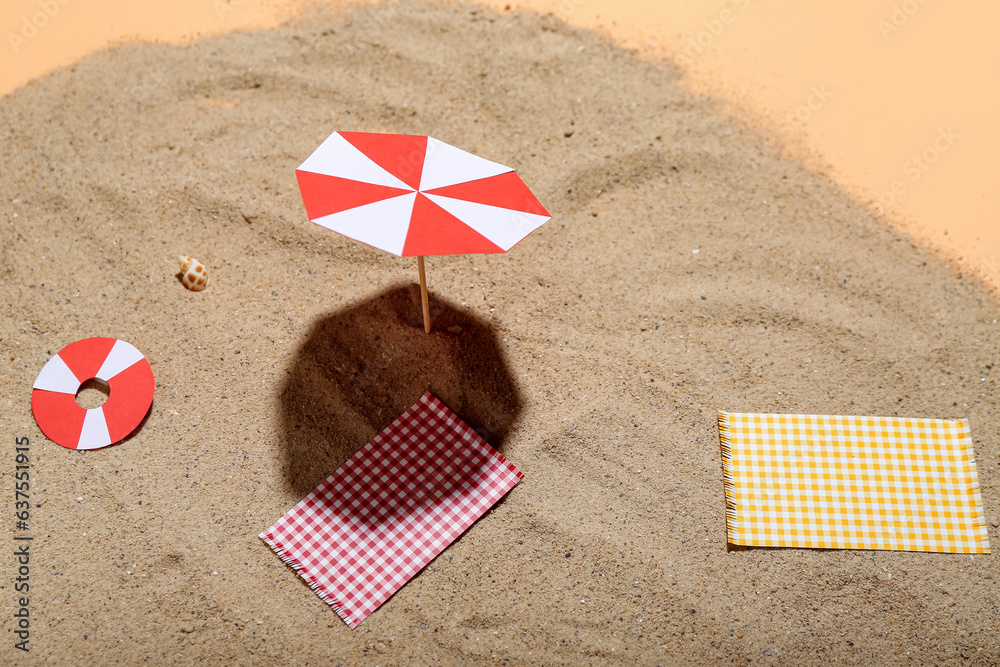 Creative summer composition with mini umbrella, beach accessories and sand on beige background