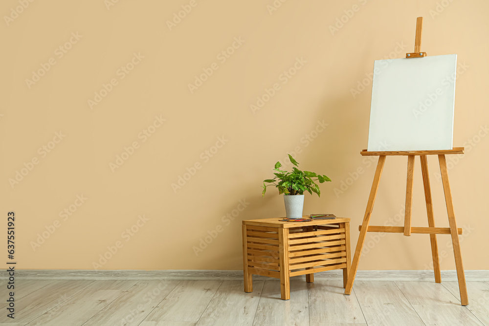 Wooden easel with blank canvas near beige wall