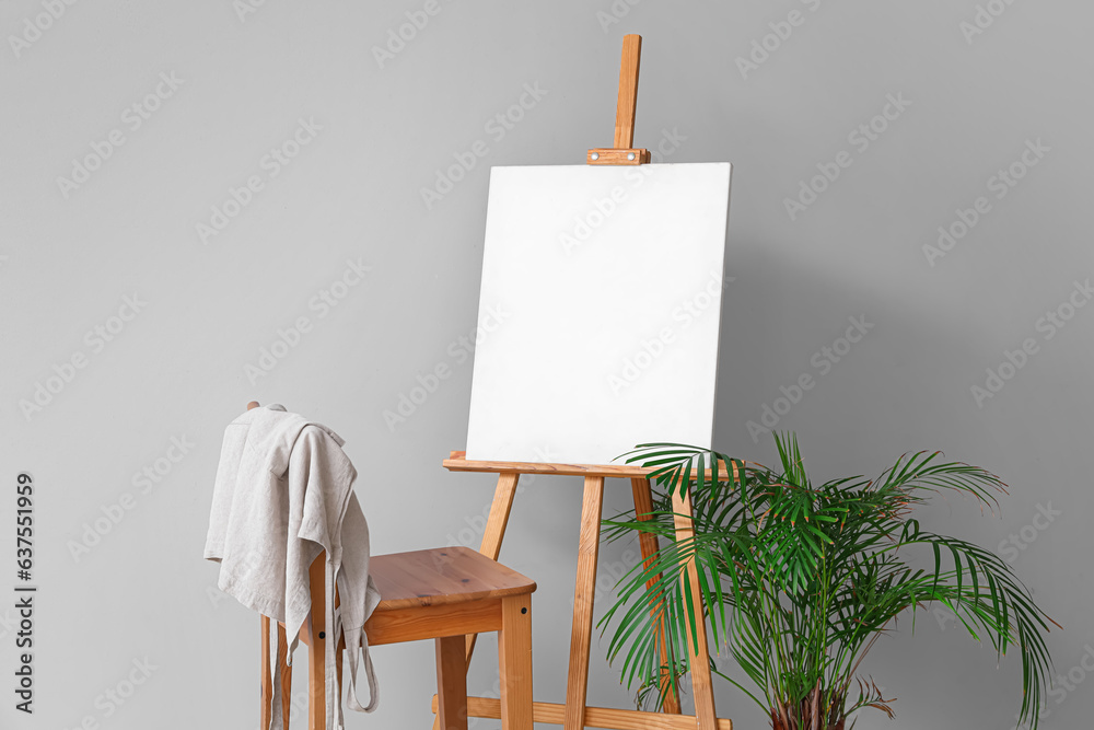 Wooden easel with blank canvas near grey wall